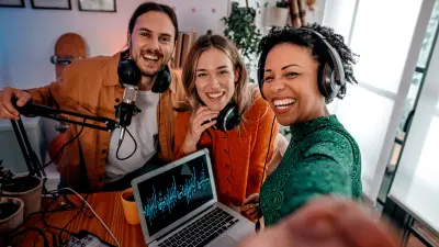 Image of three young people in an improvised podcast studio smiling at the camera