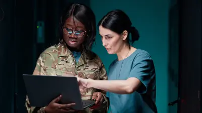 Image of two woman wearing military outfits and looking at a laptop screen together