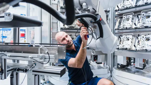 Image of male engineer, inspecting an industrial robot in a factory setting