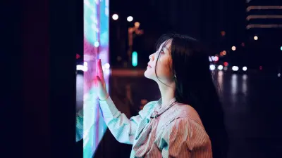 A woman touches a glowing digital screen at night, symbolizing the connection between humans, technology, and artificial intelligence.