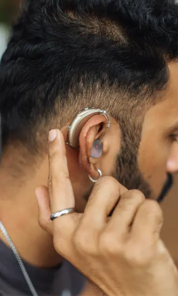 Eine junger Mann mit einem hochentwickelten medizinischen Hörgerät bedient die Hörhilfe, welche miniaturisierte PCBs enthält, um die Verbindung von Bosch mit HDI-Leiterplatten und künstlicher Intelligenz darzustellen.