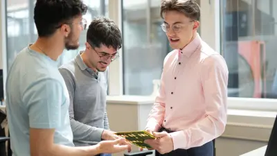 Team of three men holding a printed circuit board (PCB) discussing cost aspects