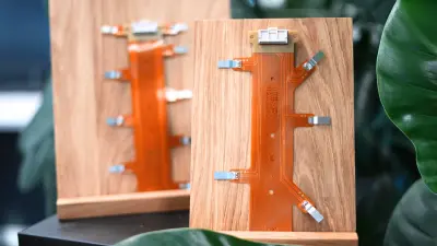 Zwei orangefarbene flexible Leiterplatten (PCBs) stehen auf einem Holzregal, umgeben von grünen Blättern, im Hauptsitz von Bosch copperdot.