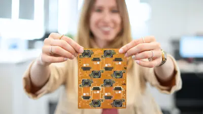 Eine Frau, die mit beiden Händen eine orangefarbene starr-flexible Leiterplatte in der Zentrale von copperdot hochhält.